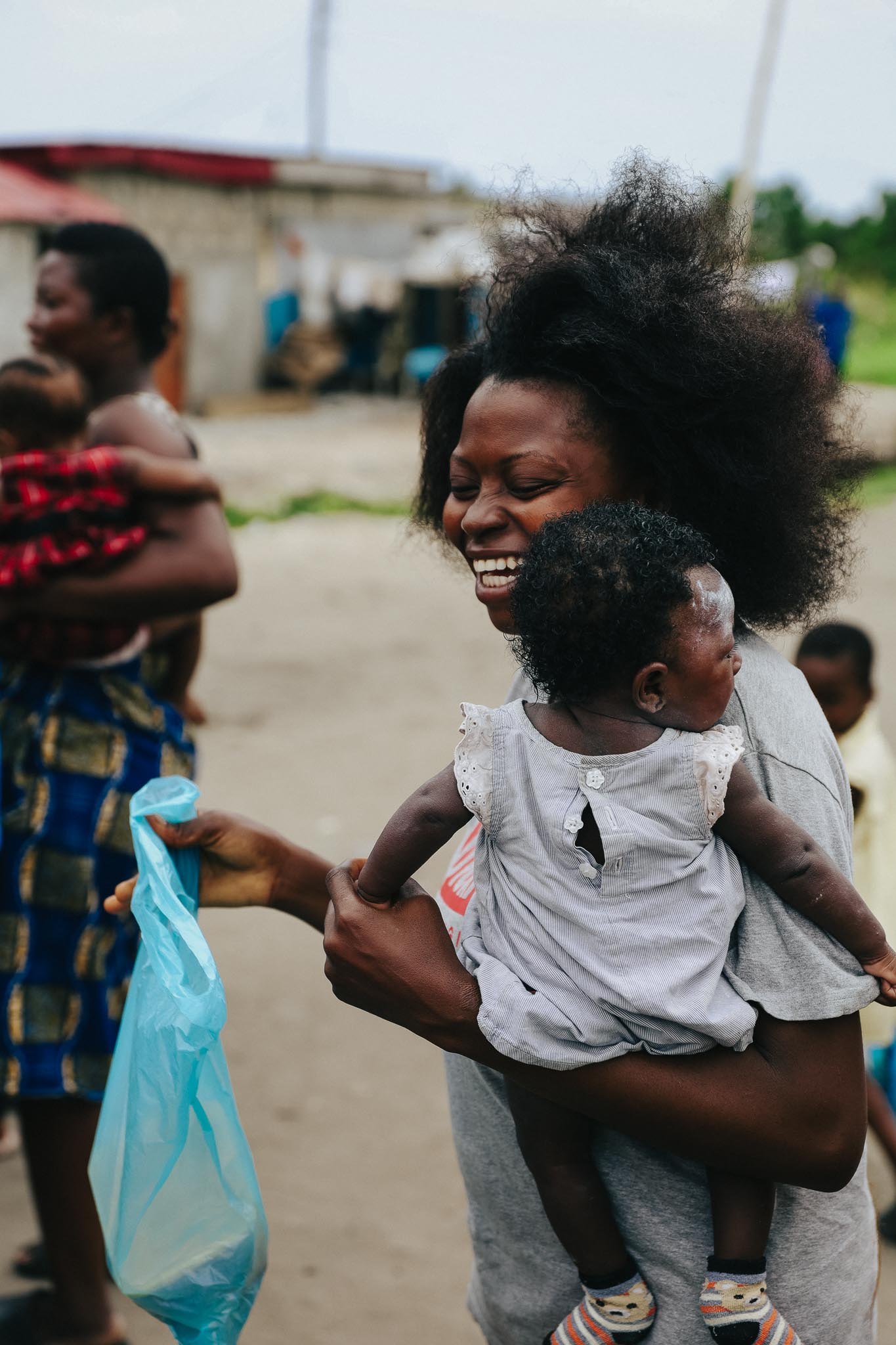A smiling mother holding her baby in one arm and a meal in the other, symbolizing hope and support provided by Hunger Relief West Africa.